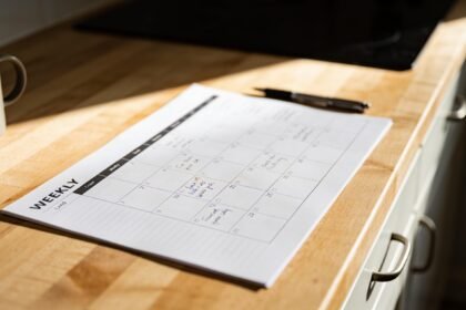 A printed one-page family week planner part-filled in on a kitchen bench beside a pen.