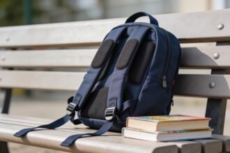 A child's backpack with its padded shoulder straps laid out flat beside a stack of school books.