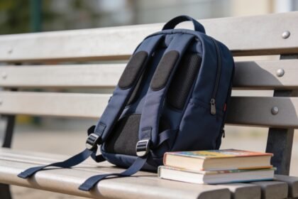 A child's backpack with its padded shoulder straps laid out flat beside a stack of school books.