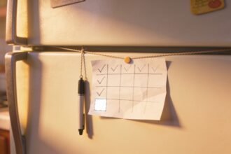 A simple hand-drawn chart stuck low on a fridge with some boxes ticked and a pen hanging beside it.
