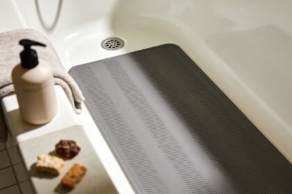 An empty bath with a rubber non-slip mat in the bottom, a folded towel and an unlabelled bottle on the edge.