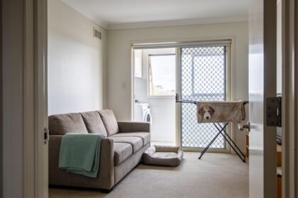 A tidy living room with a folded sofa throw, dog bed and pet blanket drying in the adjoining laundry.