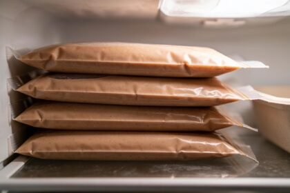 Flat sealed freezer bags of sauce stacked on their sides in a freezer drawer beside a shallow container.
