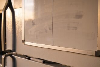 A fridge whiteboard wiped almost clean with a marker lying on the bench below, lid off.
