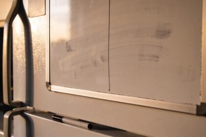 A fridge whiteboard wiped almost clean with a marker lying on the bench below, lid off.