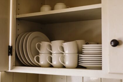 An open kitchen cupboard with matching plates and cups grouped at eye level and taller storage above.