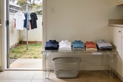 Five separate piles of clean clothing on a laundry bench, with an empty basket below and a clothesline visible outside.