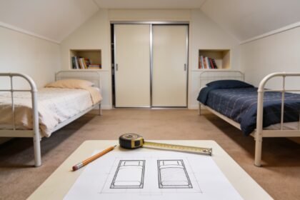 Two single beds with different bedding in a shared bedroom, with a floor-plan sketch and tape measure in the foreground.