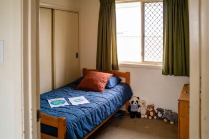 Child's bedroom with a timber bed, blue bedding, green curtains and planet drawings ready to display.