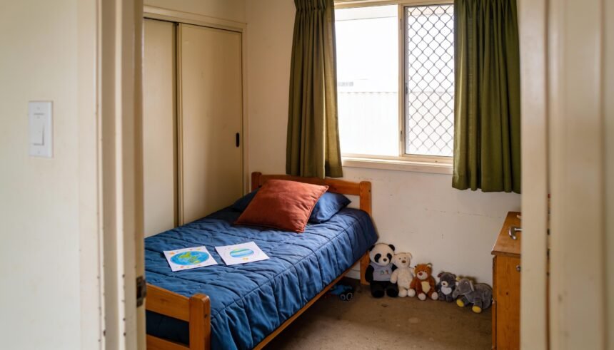 Child's bedroom with a timber bed, blue bedding, green curtains and planet drawings ready to display.
