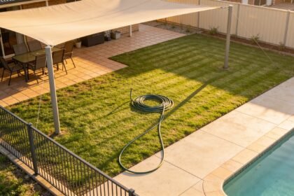 A suburban backyard in spring with a shade sail, mown lawn and a pool fence with clear space around it.