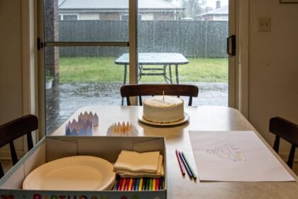 Indoor birthday table and packed activity box beside glass doors overlooking a rain-soaked backyard.
