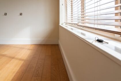 An empty rental living room with bare timber floorboards and a set of keys left on the windowsill.