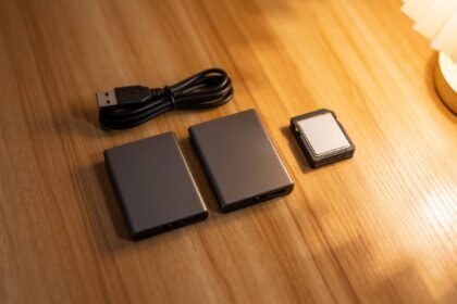 Two small external hard drives, a coiled USB cable and a stack of memory cards on a timber desk.
