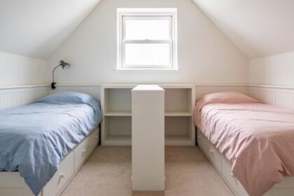 A shared children's bedroom with two single beds either side of a low white shelf unit used as a divider.
