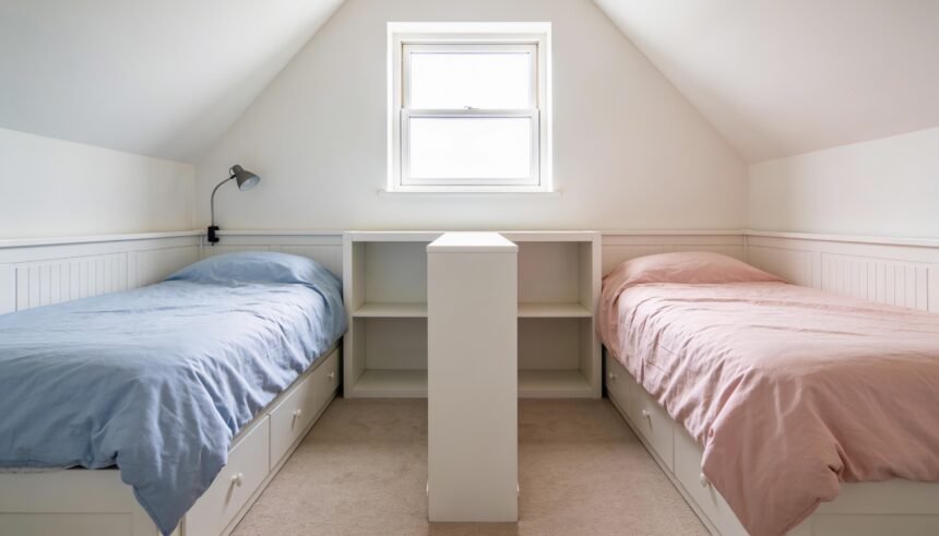 A shared children's bedroom with two single beds either side of a low white shelf unit used as a divider.