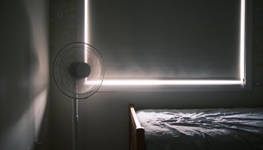 A child's bedroom with a blockout blind down over the window and a pedestal fan in the corner.