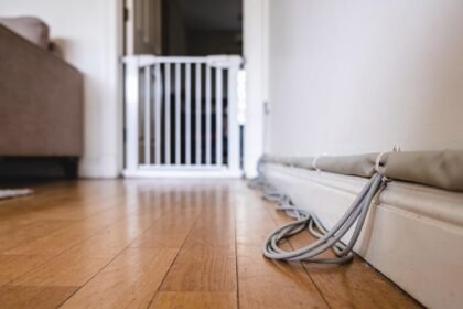 A low view along a lounge room floor towards a baby gate fitted across a doorway, with cables routed along the skirting.
