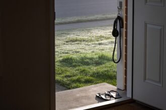An open back door at dawn looking onto a dewy lawn, with a dog lead hanging beside the door and thongs on the step.