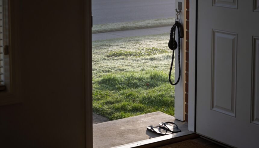 An open back door at dawn looking onto a dewy lawn, with a dog lead hanging beside the door and thongs on the step.