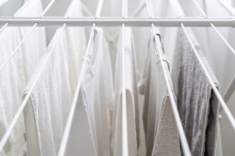 The upper rails of a white folding clothes airer hung with towels and t-shirts spaced apart with gaps of empty rail between them.