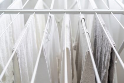 The upper rails of a white folding clothes airer hung with towels and t-shirts spaced apart with gaps of empty rail between them.