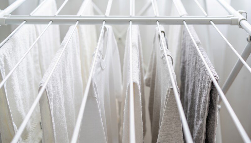 The upper rails of a white folding clothes airer hung with towels and t-shirts spaced apart with gaps of empty rail between them.