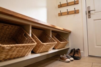 A low storage bench inside a back door with three open baskets underneath, hooks at two heights above, and adult and child shoes on the floor.