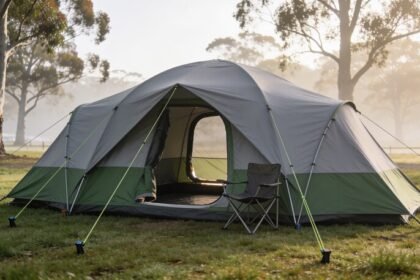 A large grey and green family dome tent pitched on grass with guy ropes pegged out taut and a folding camp chair standing in the open doorway.