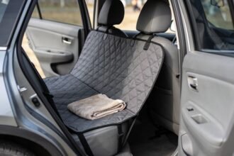 A quilted charcoal hammock cover fitted across a car's rear seat and slung up to the front headrests, with a folded towel on top.