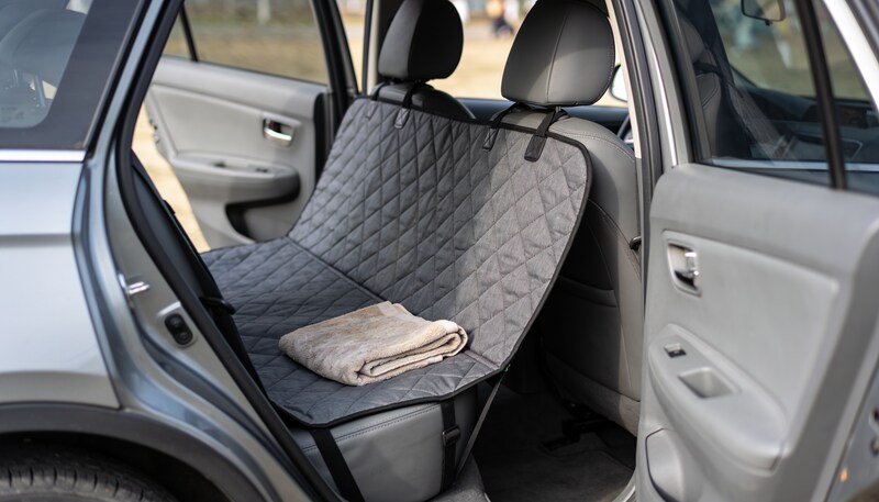 A quilted charcoal hammock cover fitted across a car's rear seat and slung up to the front headrests, with a folded towel on top.