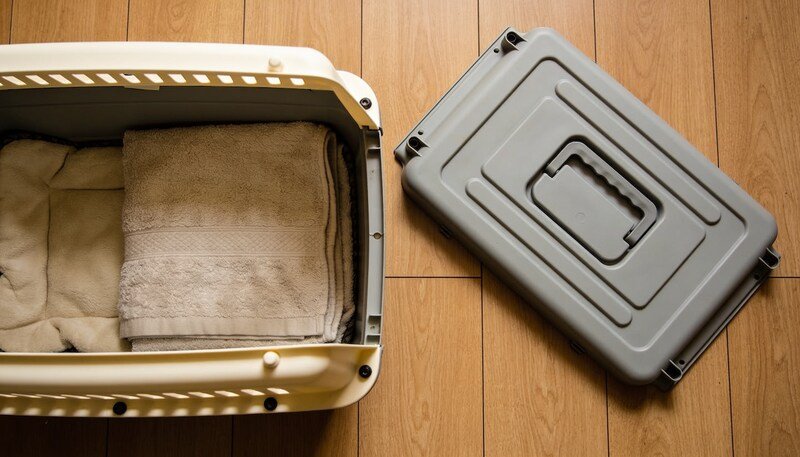 The two halves of a hard-sided pet carrier lying apart on floorboards, with a folded blanket in the lower base and the upper half beside it.