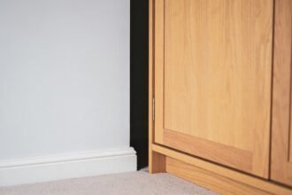 A timber wardrobe pulled away from a pale bedroom wall, showing the dark gap of air between it and the skirting board.