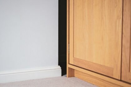 A timber wardrobe pulled away from a pale bedroom wall, showing the dark gap of air between it and the skirting board.