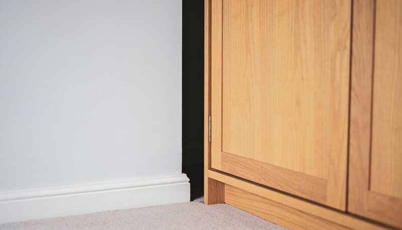 A timber wardrobe pulled away from a pale bedroom wall, showing the dark gap of air between it and the skirting board.
