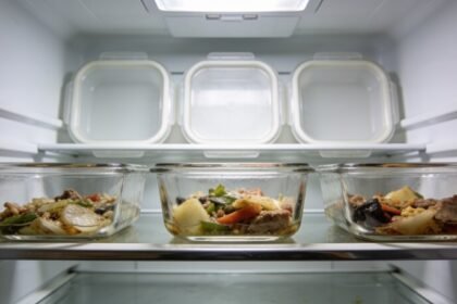 Three clear glass containers of leftovers sitting together at the front of a fridge shelf, with their lids set on the shelf above.