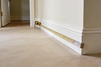 A tape measure extended across an empty corner of a room, measuring the space near a skirting board.