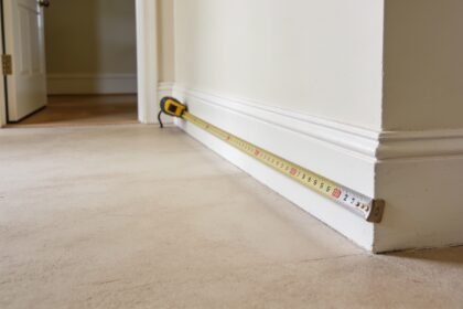 A tape measure extended across an empty corner of a room, measuring the space near a skirting board.