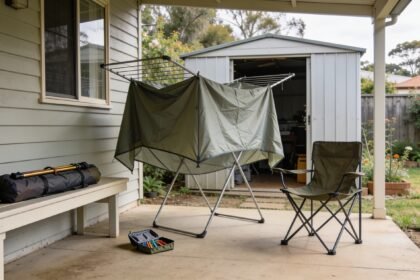 Tent fabric airing on a verandah beside a shed, with poles, pegs and a camping chair being sorted nearby.