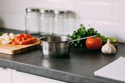 A kitchen bench with a separate cutting board and pot set apart while a meal is prepared.