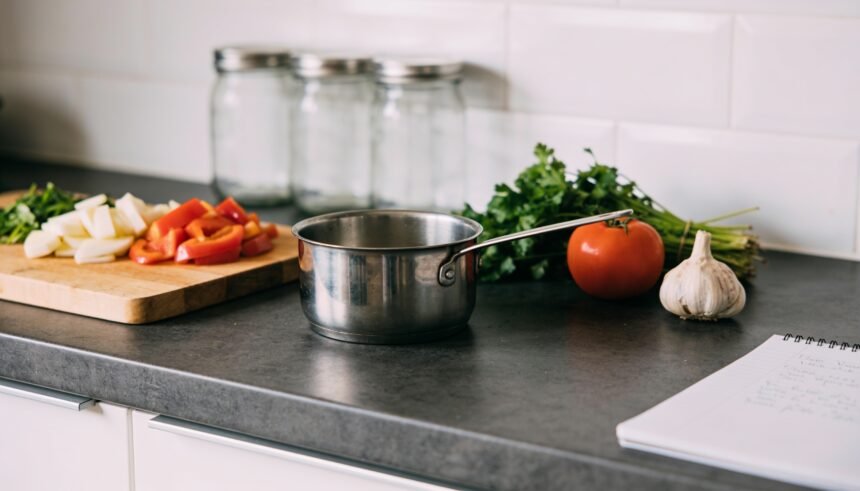 A kitchen bench with a separate cutting board and pot set apart while a meal is prepared.