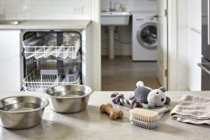 A stainless steel pet bowl, a water bowl and a rubber, rope and plush toy laid out on a kitchen bench ready for washing.
