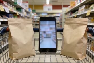 Two grocery packs beside a shopping basket and smartphone in a supermarket aisle.