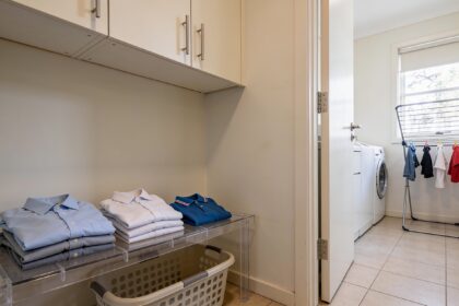 Adult work shirts and school polos on a laundry bench beside an empty basket, with clothes drying on an airer nearby.