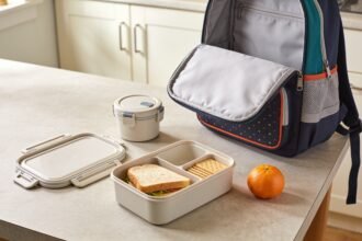 Compartment lunchbox and closed snack pot arranged beside a lunch bag and school backpack.
