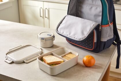 Compartment lunchbox and closed snack pot arranged beside a lunch bag and school backpack.